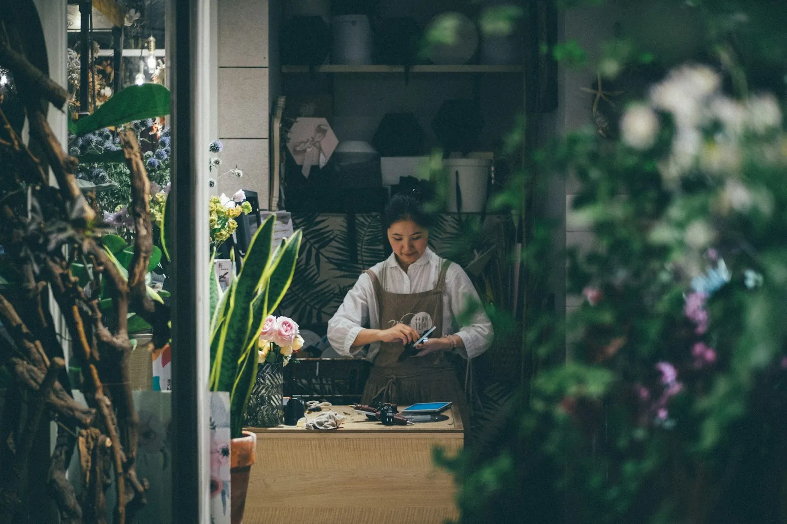 Fiorista al lavoro dietro il bancone tra piante e fiori