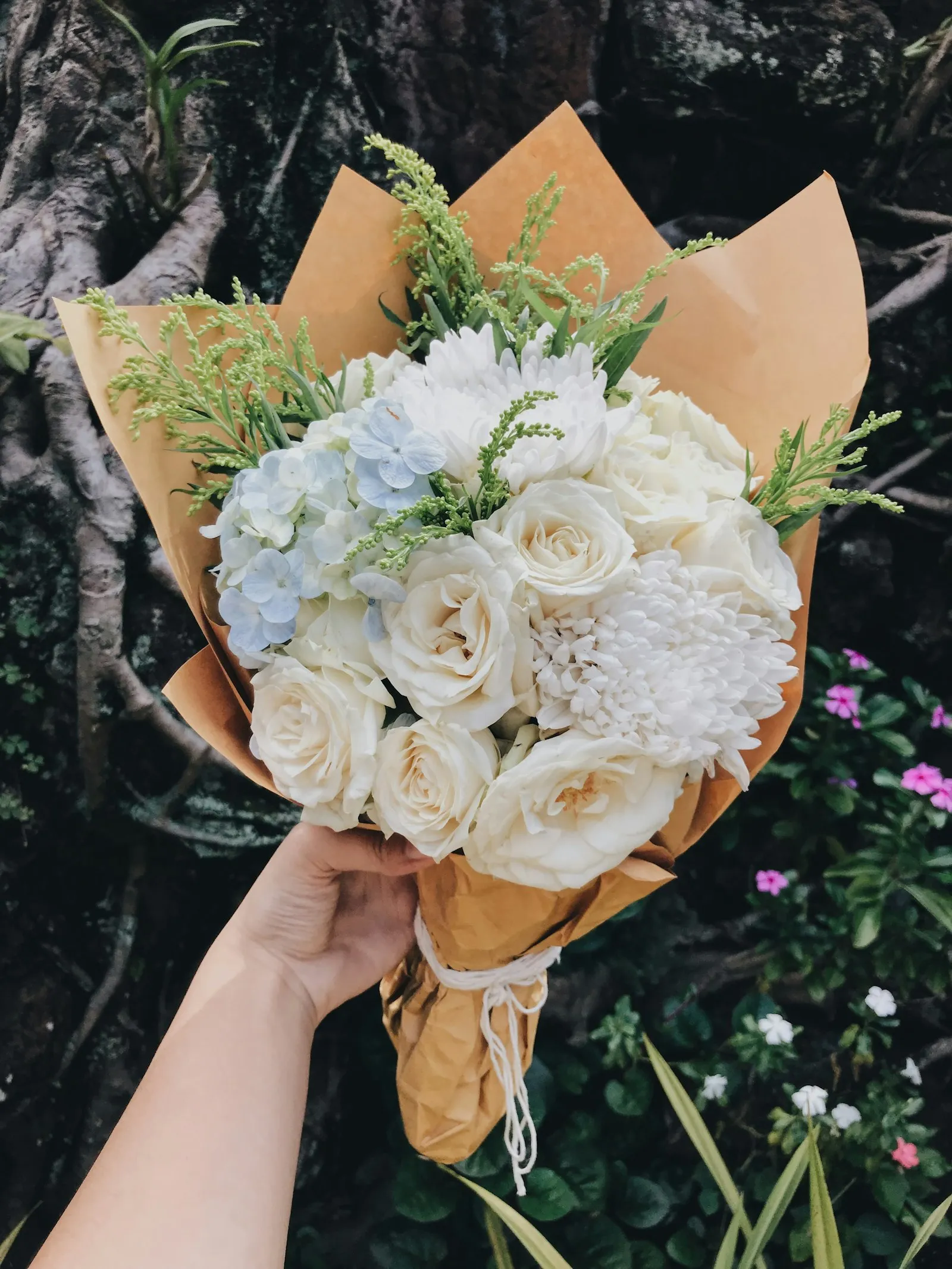 Mano che tiene un bouquet di rose bianche avvolto in carta da pacco