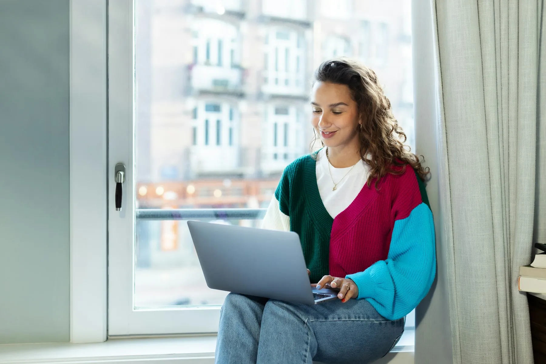 Una libera professionista lavora al computer seduta sul davanzale